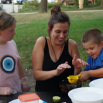 Na zdjęciu uśmiechnięci prowadząca i dwójka dzieci, wyciskają sok z cytryny.