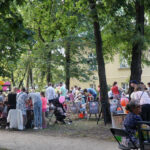 3. Na zdjęciu widzimy grupę ludzi znajdujących się w parku. Ludzie uczestniczą w pikniku z okazji 4 urodzin Miejsca Aktywności Lokalnej przy CKiA. Widzimy również balony rozwieszone przy drzewach.